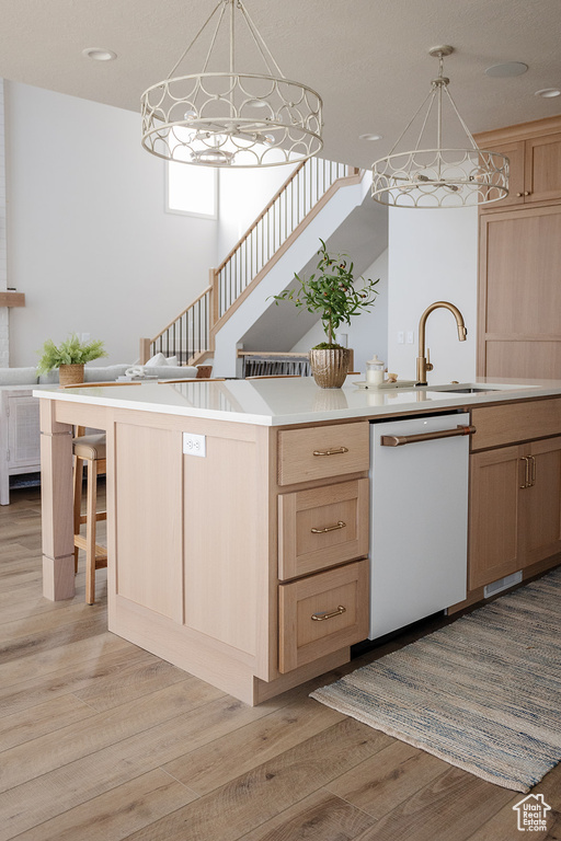 Kitchen featuring white dishwasher, light brown cabinets, light wood-style floors, light countertops, and decorative light fixtures