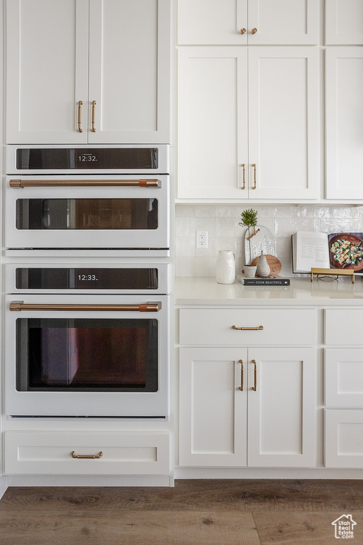 Kitchen featuring white double oven, white cabinetry, light countertops, and tasteful backsplash