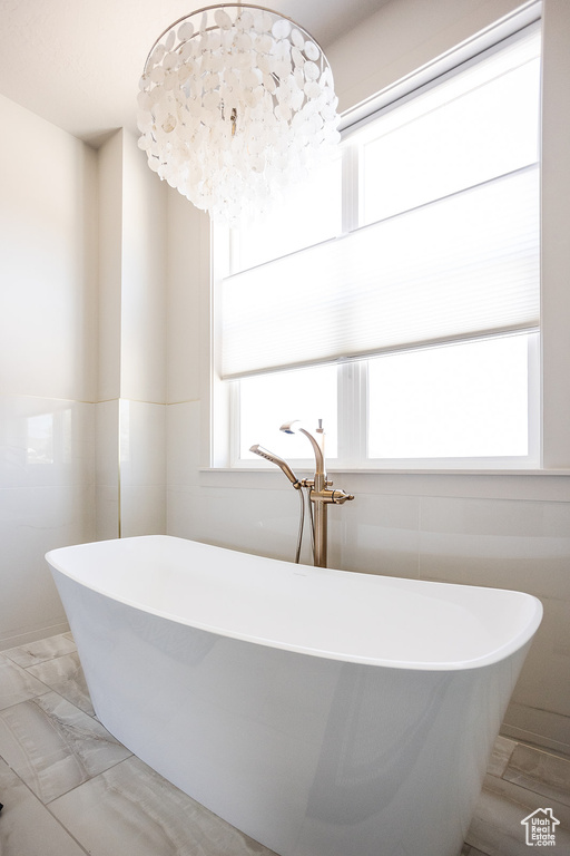Full bathroom featuring a freestanding bath, marble look tiles, tile walls, and a chandelier