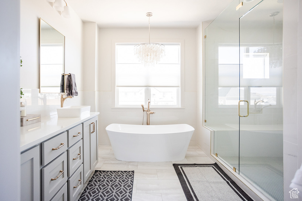 Full bath with vanity, a freestanding tub, a chandelier, a shower stall, and marble finish flooring
