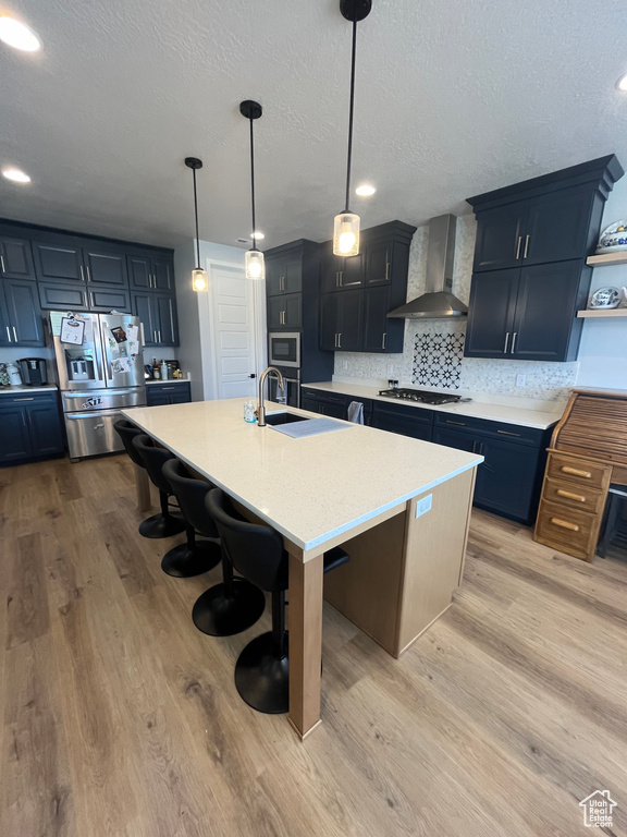 Kitchen with appliances with stainless steel finishes, wall chimney exhaust hood, open shelves, a kitchen bar, and light countertops