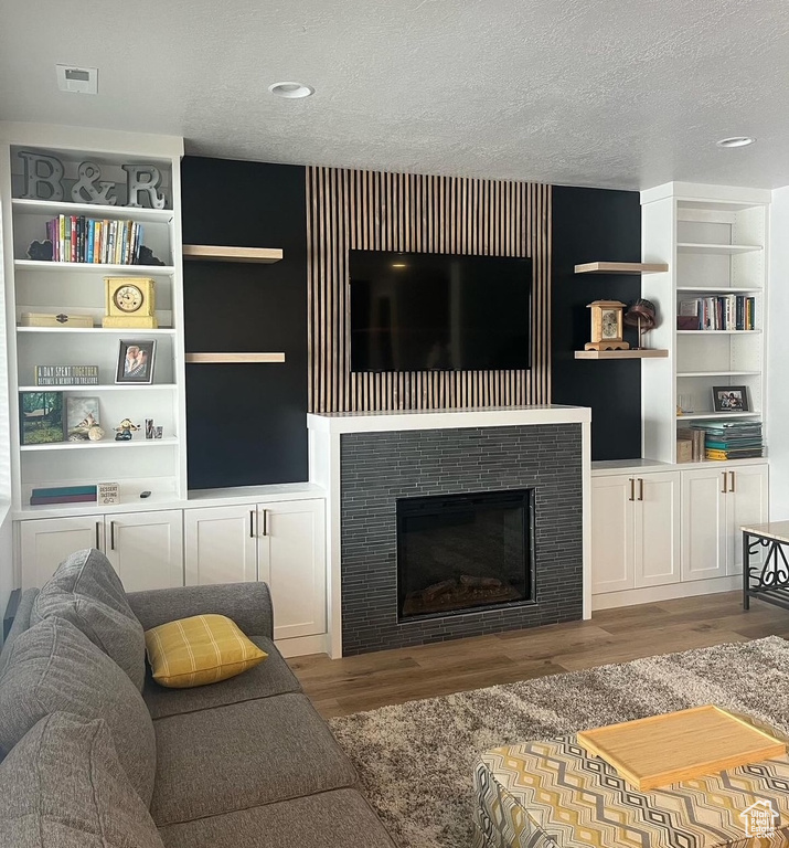 Living room with a textured ceiling, wood finished floors, a tile fireplace, and built in features