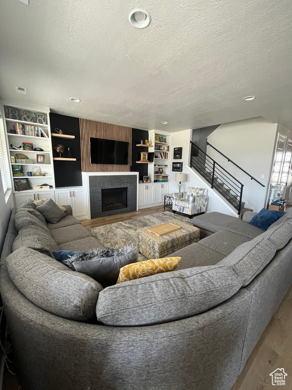 Living area with wood finished floors, a textured ceiling, a fireplace, stairway, and built in shelves