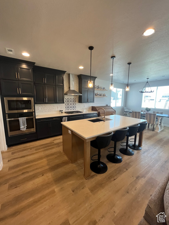 Kitchen with wall chimney range hood, gas stovetop, a sink, a breakfast bar, and dark cabinetry