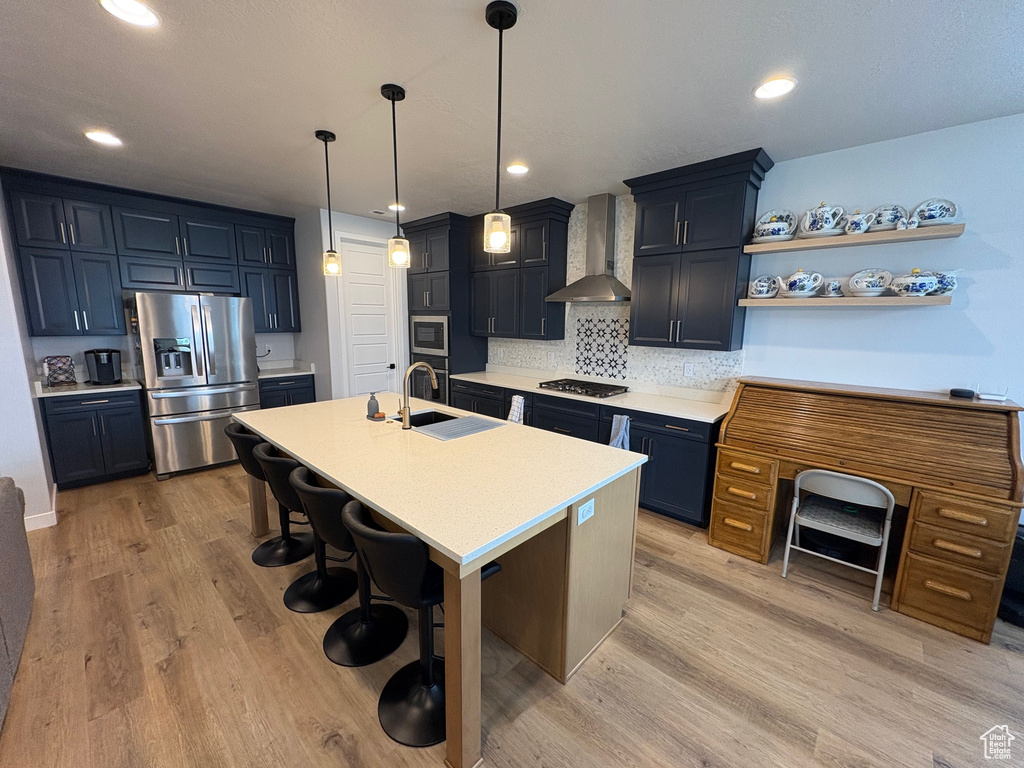 Kitchen with stainless steel appliances, wall chimney exhaust hood, a sink, light countertops, and a breakfast bar area