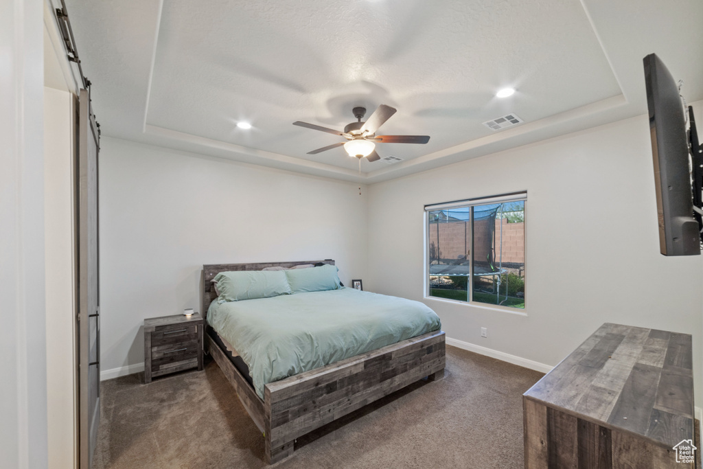 Bedroom featuring dark carpet, a tray ceiling, baseboards, recessed lighting, and ceiling fan