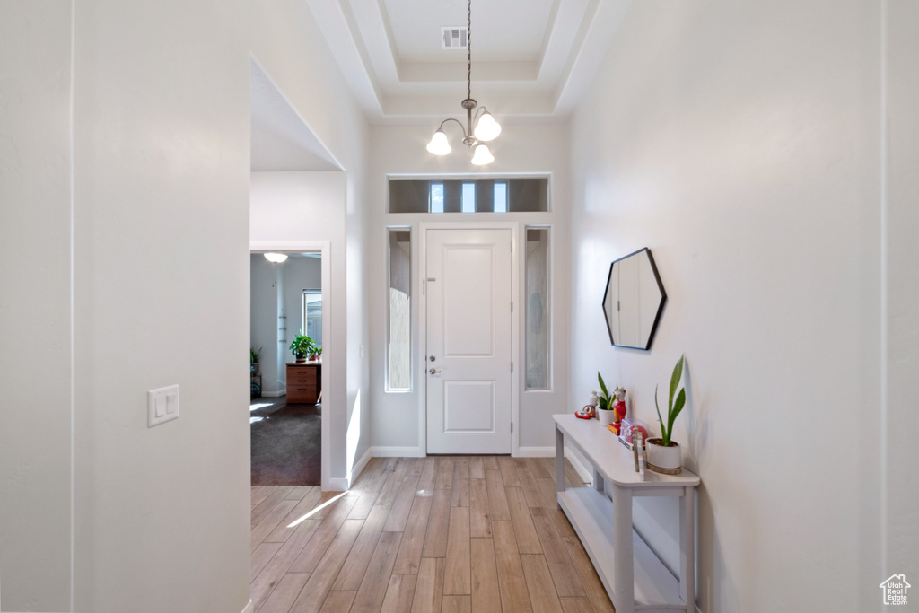 Entrance foyer featuring light wood finished floors, baseboards, a chandelier, and a tray ceiling