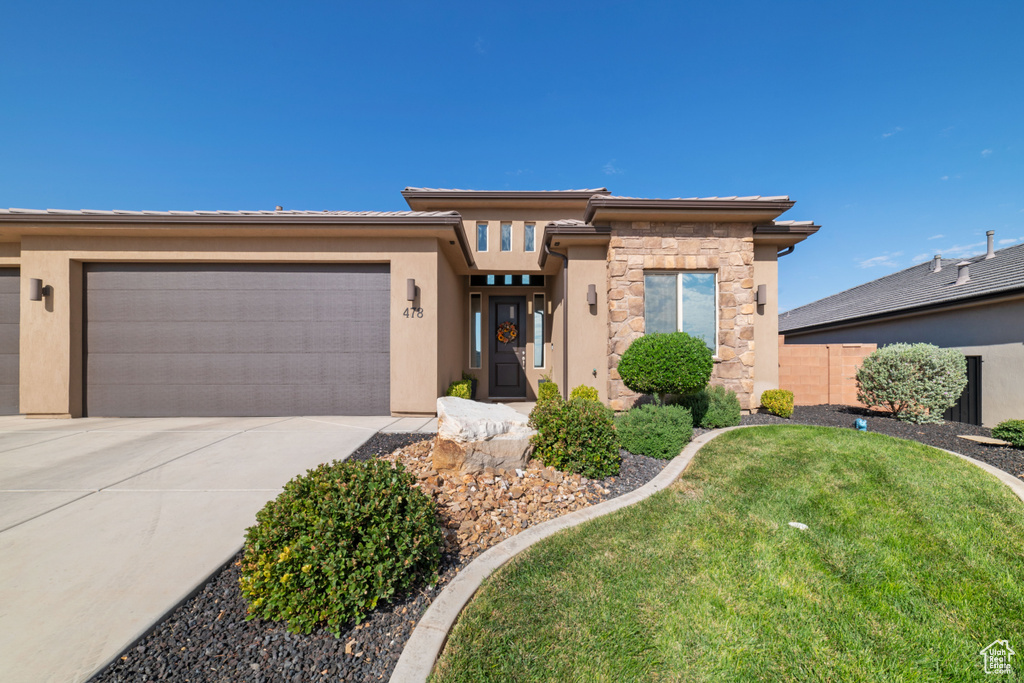 Prairie-style home featuring an attached garage, concrete driveway, stone siding, and stucco siding