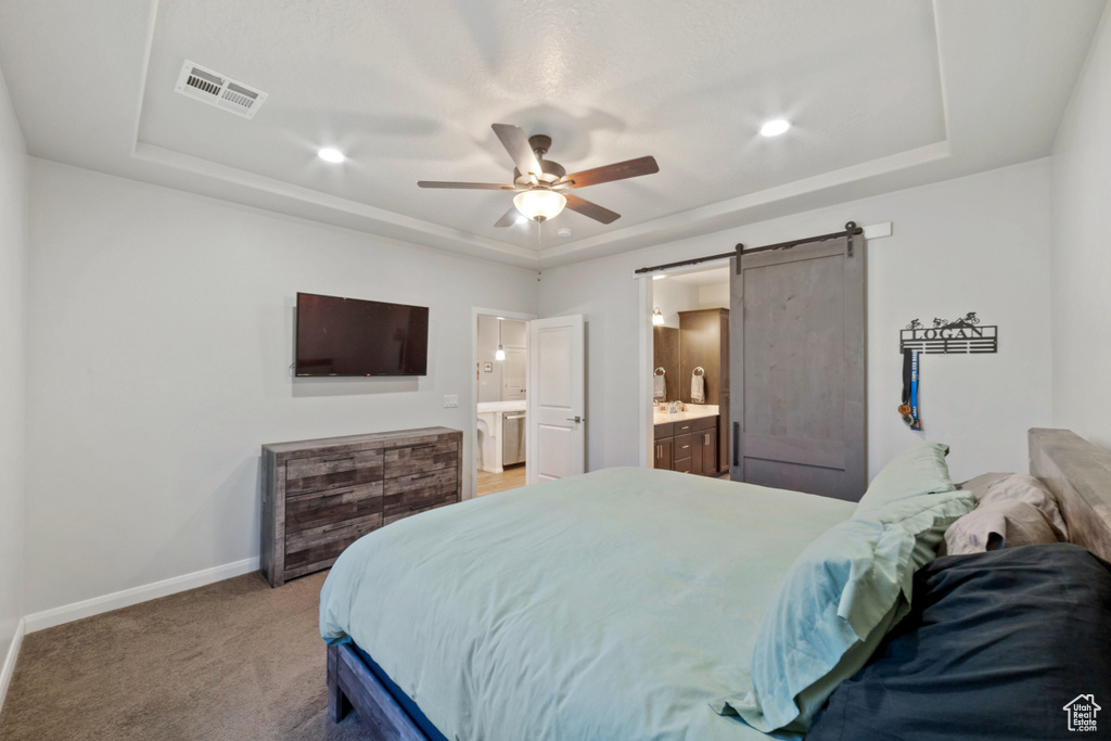 Bedroom with a raised ceiling, a barn door, baseboards, ensuite bath, and recessed lighting