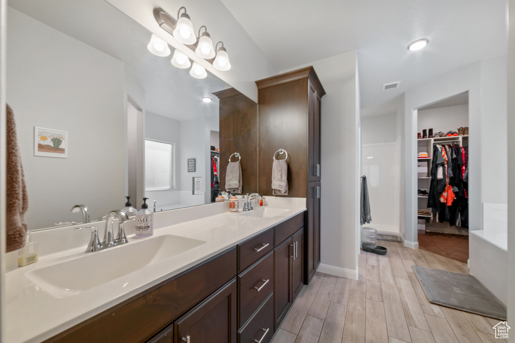 Full bathroom with double vanity, a walk in closet, wood finished floors, baseboards, and recessed lighting