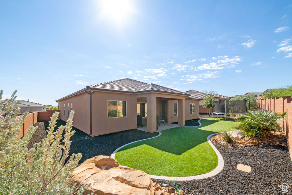 Back of property featuring a trampoline, a tiled roof, a patio area, and stucco siding
