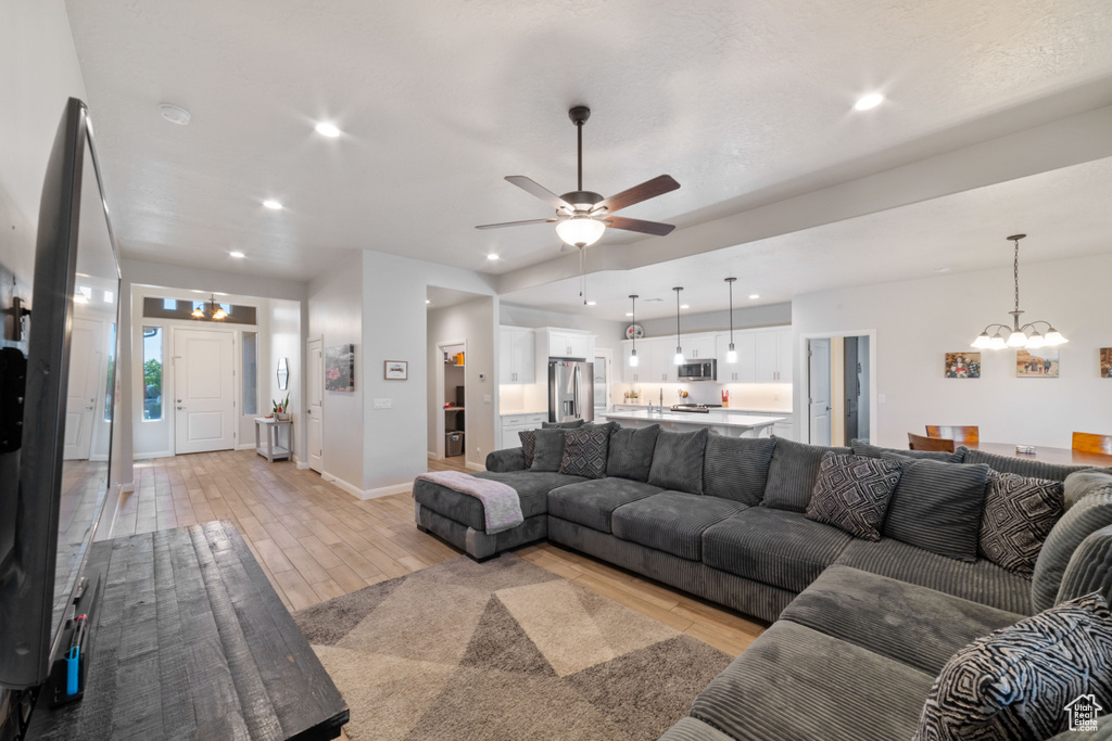 Living room with a chandelier, light wood-type flooring, a ceiling fan, recessed lighting, and baseboards