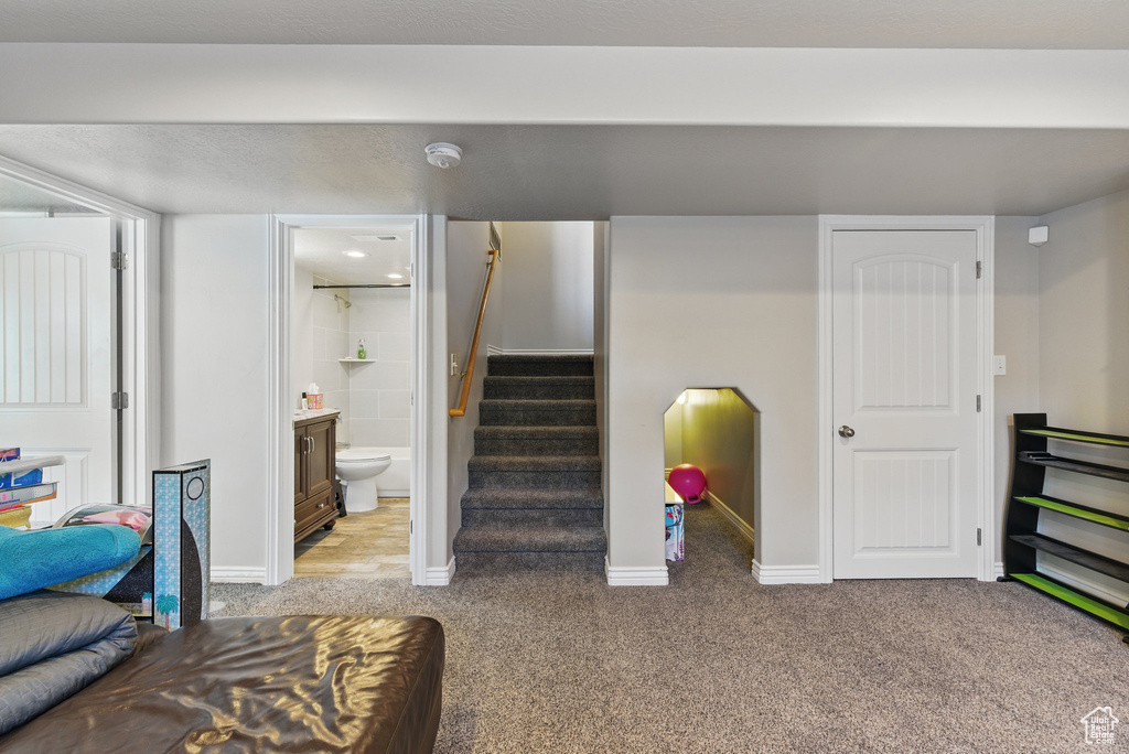 Below grade area featuring light colored carpet, stairway, and baseboards