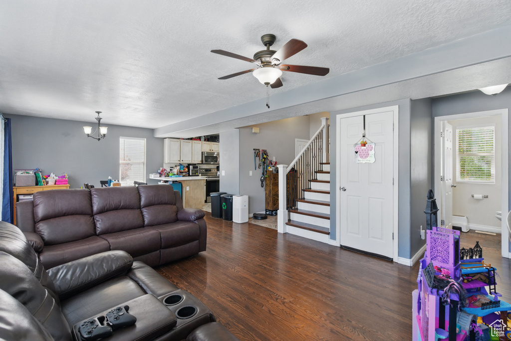 Living area featuring stairway, ceiling fan, a chandelier, dark wood-style floors, and baseboards