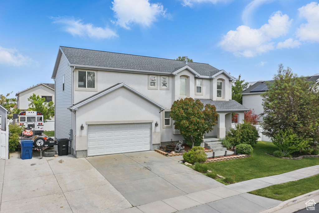 Traditional-style house featuring a garage, a front lawn, stucco siding, a shingled roof, and driveway