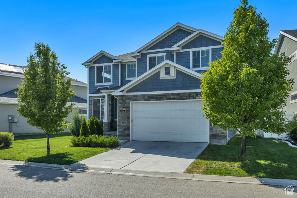 Craftsman-style home featuring stone siding, driveway, a front lawn, an attached garage, and board and batten siding