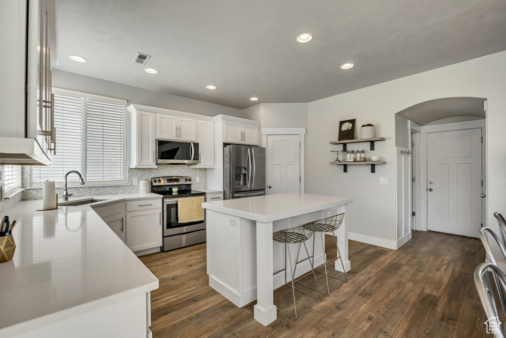 Kitchen with appliances with stainless steel finishes, a sink, tasteful backsplash, dark wood-type flooring, and a center island
