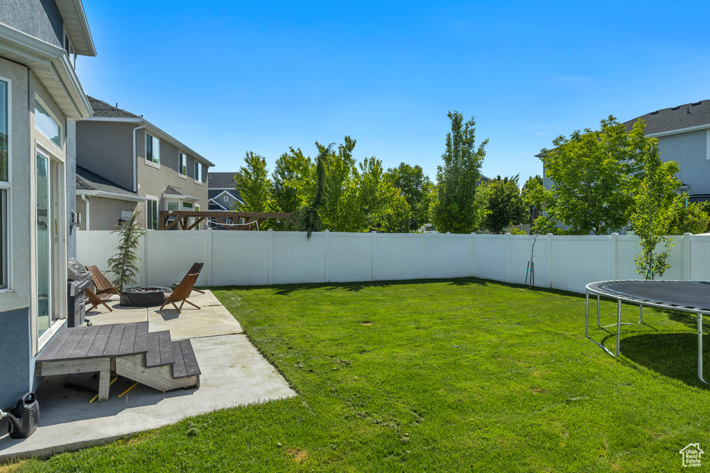 View of yard featuring a trampoline, a fire pit, and a patio area