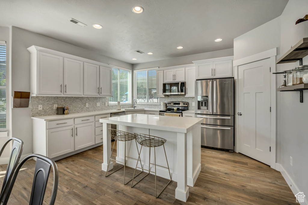 Kitchen with appliances with stainless steel finishes, a sink, tasteful backsplash, white cabinetry, and a breakfast bar