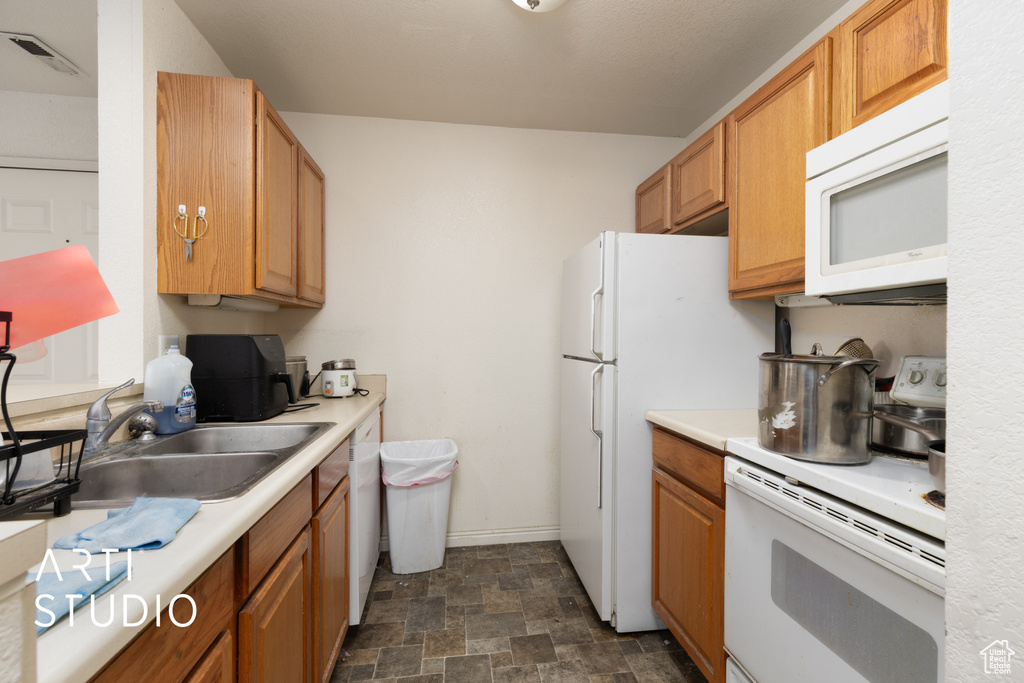 Kitchen with white appliances, a sink, light countertops, and stone finish floors