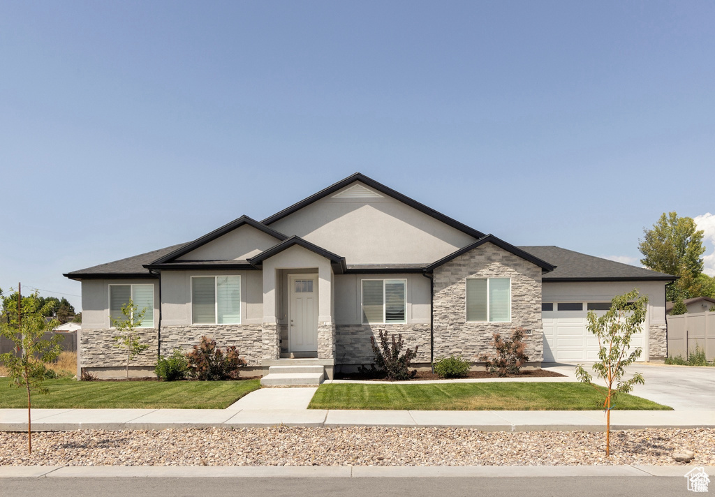View of front of property with stone siding, an attached garage, stucco siding, and driveway