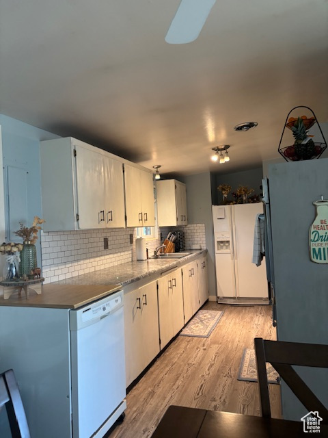 Kitchen with white appliances, decorative backsplash, light wood-style flooring, a sink, and white cabinets