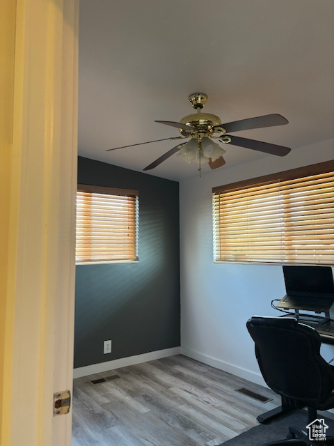 Home office with ceiling fan, healthy amount of natural light, wood finished floors, and baseboards