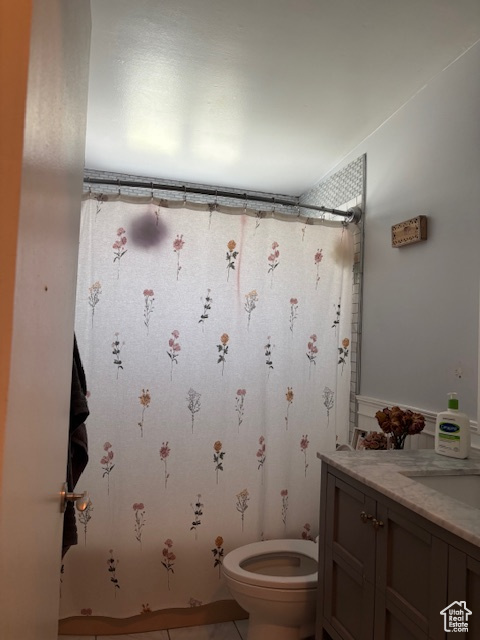 Full bath with toilet, vanity, curtained shower, tile patterned floors, and wainscoting