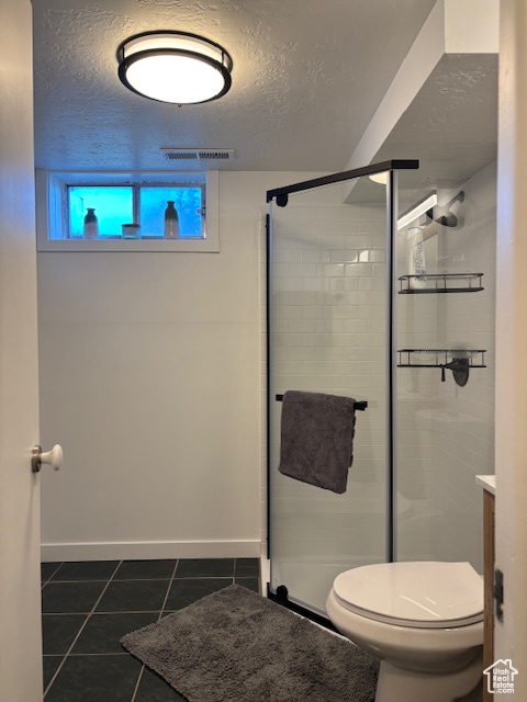 Bathroom featuring tile patterned flooring, toilet, a stall shower, a textured ceiling, and baseboards