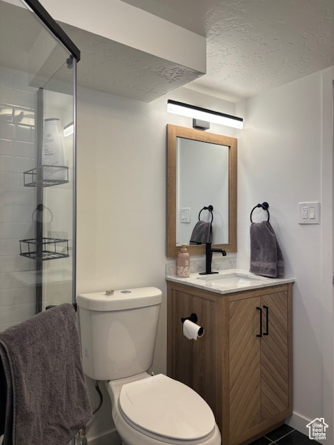 Bathroom featuring vanity, toilet, a textured ceiling, a stall shower, and tile patterned floors