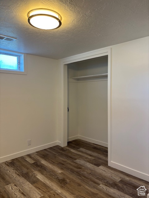 Unfurnished bedroom featuring dark wood finished floors, a closet, a textured ceiling, and baseboards