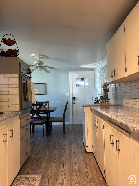 Kitchen featuring ceiling fan, backsplash, black oven, dark wood-style flooring, and white cabinetry