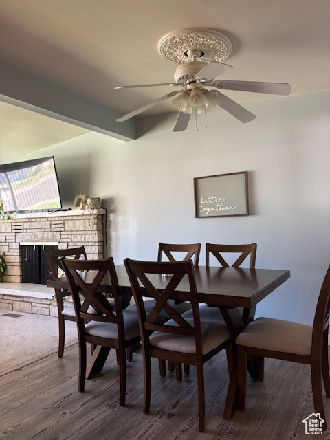 Dining space featuring ceiling fan, a stone fireplace, and wood finished floors