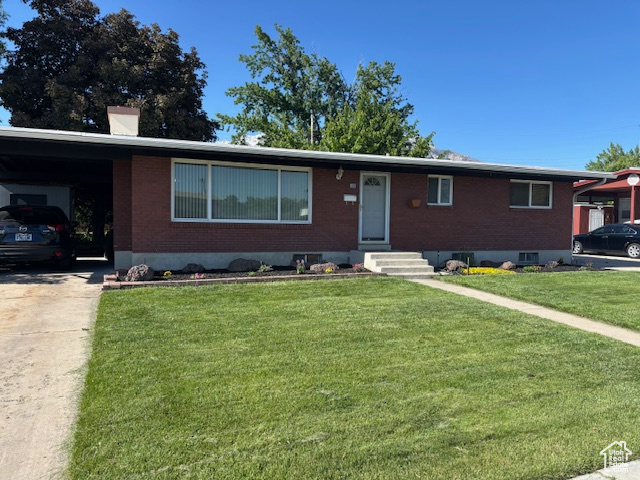 Ranch-style house featuring brick siding, a front lawn, concrete driveway, and a chimney