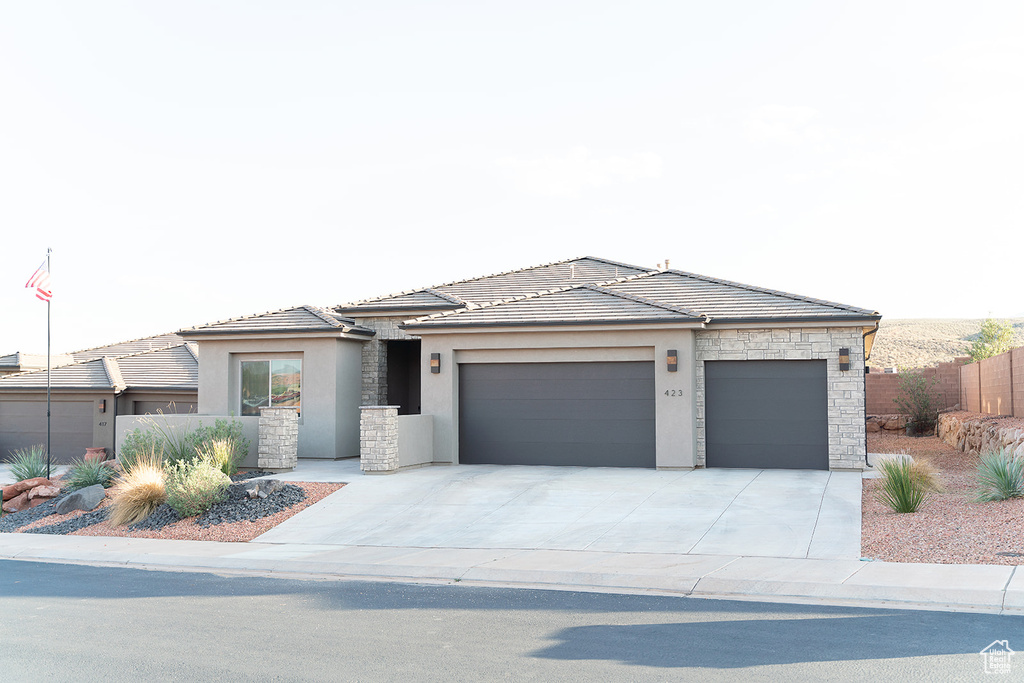 Prairie-style house featuring stucco siding, stone siding, an attached garage, and concrete driveway