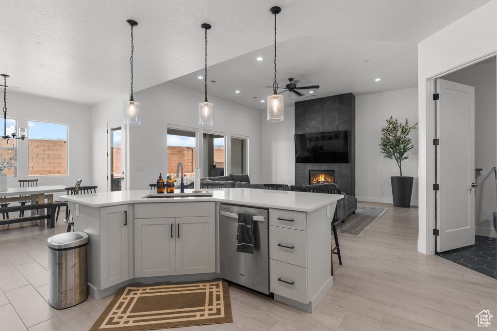 Kitchen with stainless steel dishwasher, a sink, ceiling fan, light countertops, and a large fireplace