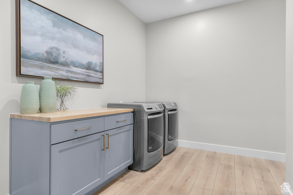 Laundry room featuring washing machine and clothes dryer, baseboards, light wood-style floors, and cabinet space
