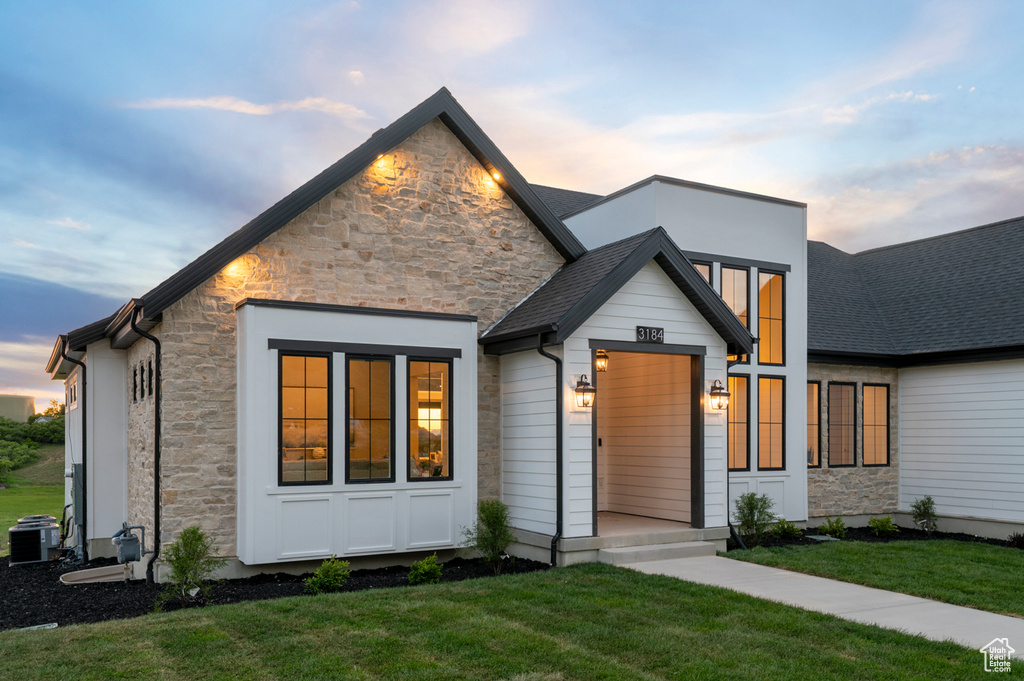 View of front of house with stone siding, a lawn, and central AC