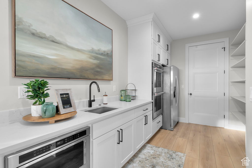 Kitchen featuring a sink, stainless steel appliances, white cabinets, light countertops, and recessed lighting