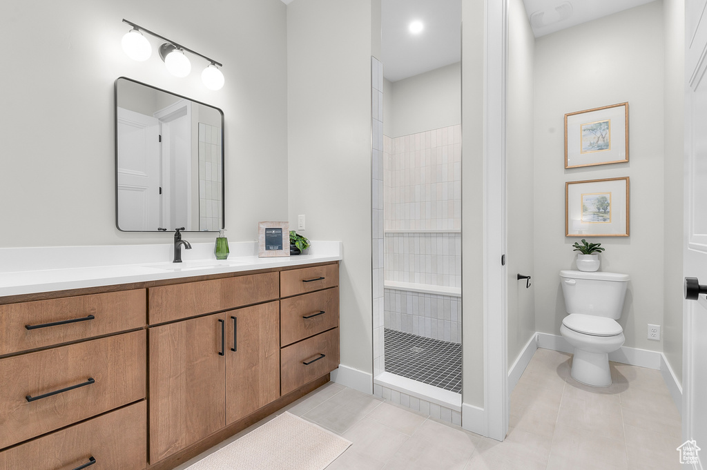 Bathroom with a tile shower, toilet, tile patterned flooring, and vanity