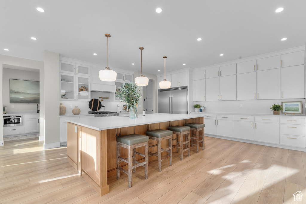 Kitchen with built in fridge, a large island, light wood finished floors, recessed lighting, and white cabinets
