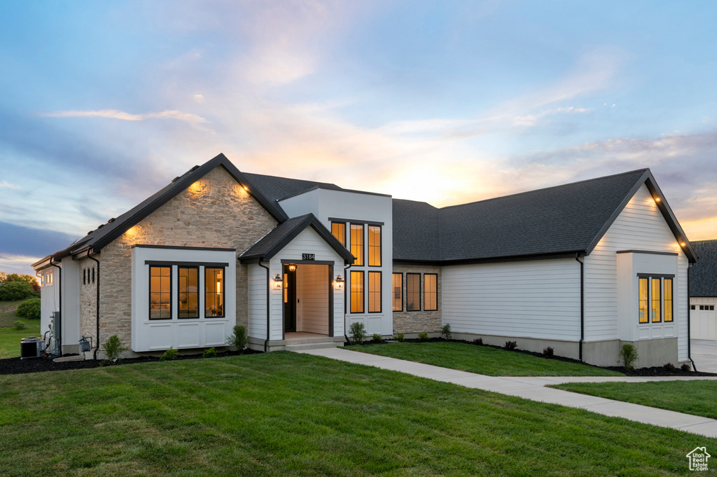 View of front facade with stone siding, a lawn, and central AC unit