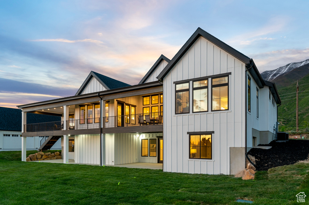Back of house with board and batten siding, a lawn, stairway, a patio area, and central air condition unit