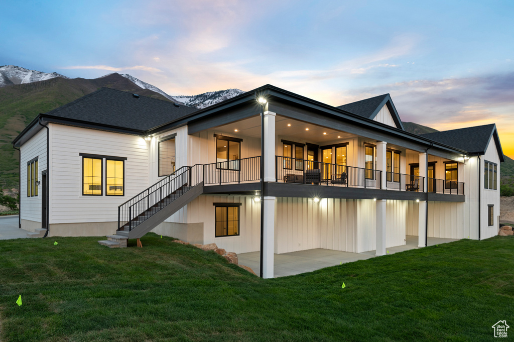Back of house at dusk with a patio, a yard, stairway, and a mountain view
