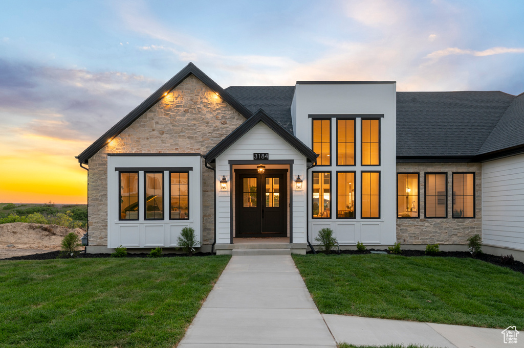 View of front of home with stone siding, a lawn, and a shingled roof