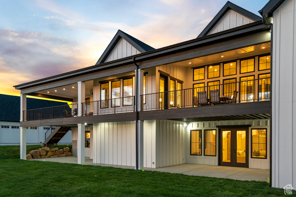 Back of house with board and batten siding, a lawn, french doors, and a patio area