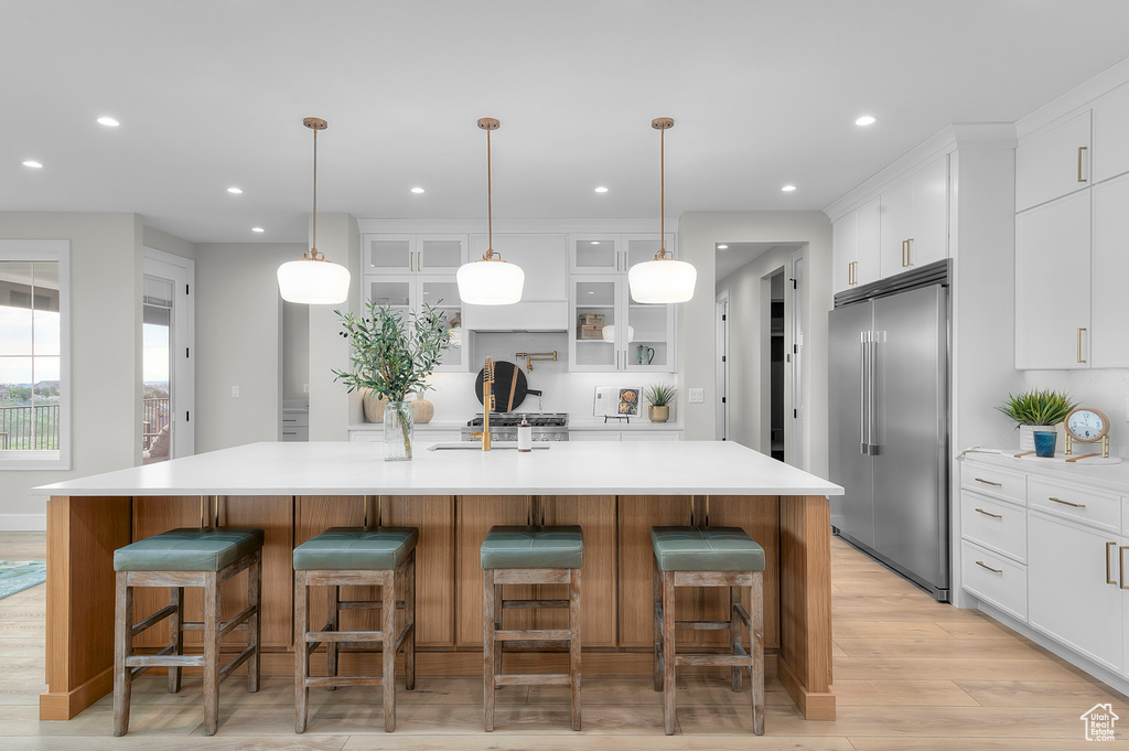 Kitchen with built in refrigerator, a sink, light wood-type flooring, white cabinetry, and glass insert cabinets