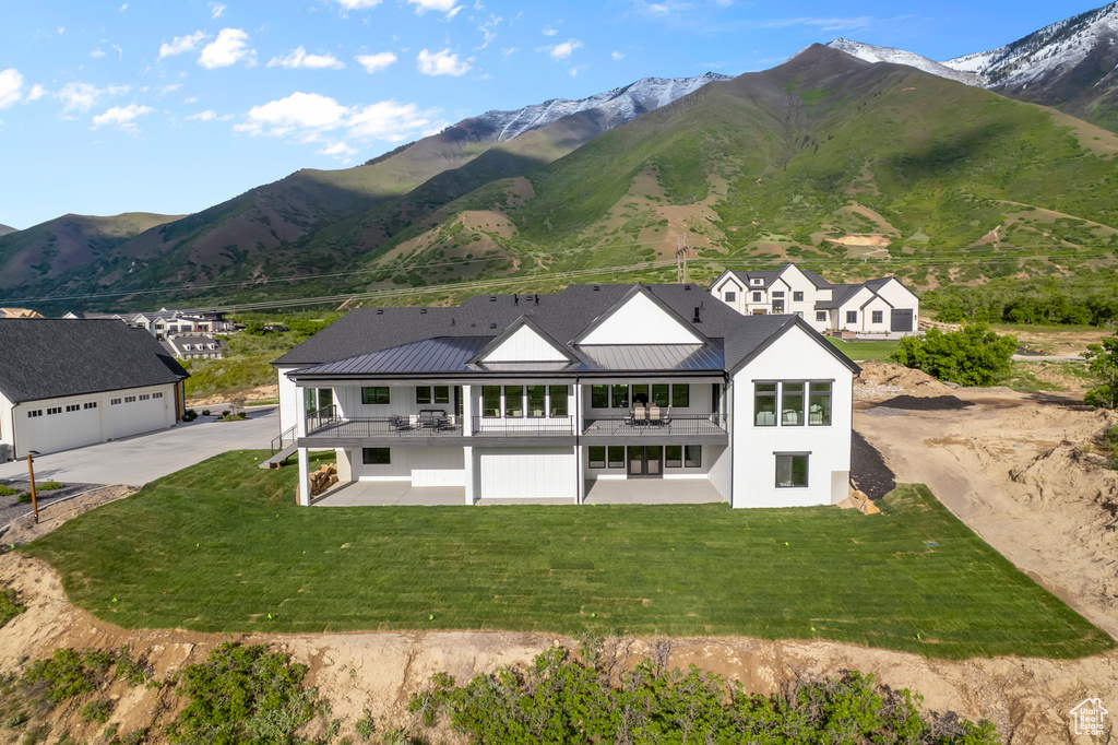 Rear view of property featuring a balcony, concrete driveway, a yard, a mountain view, and metal roof