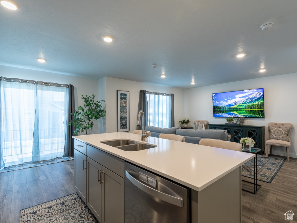 Kitchen with dishwasher, a sink, dark wood finished floors, light countertops, and recessed lighting