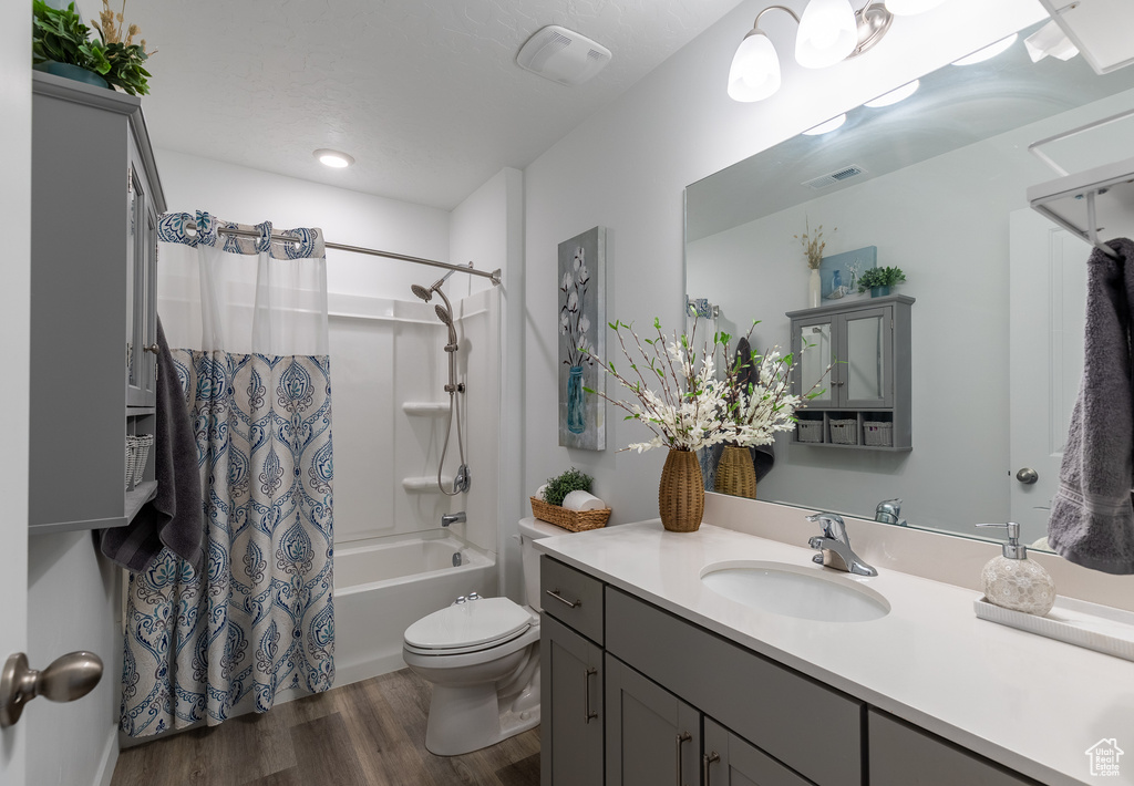 Full bathroom featuring wood finished floors, vanity, shower / bathtub combination with curtain, and toilet